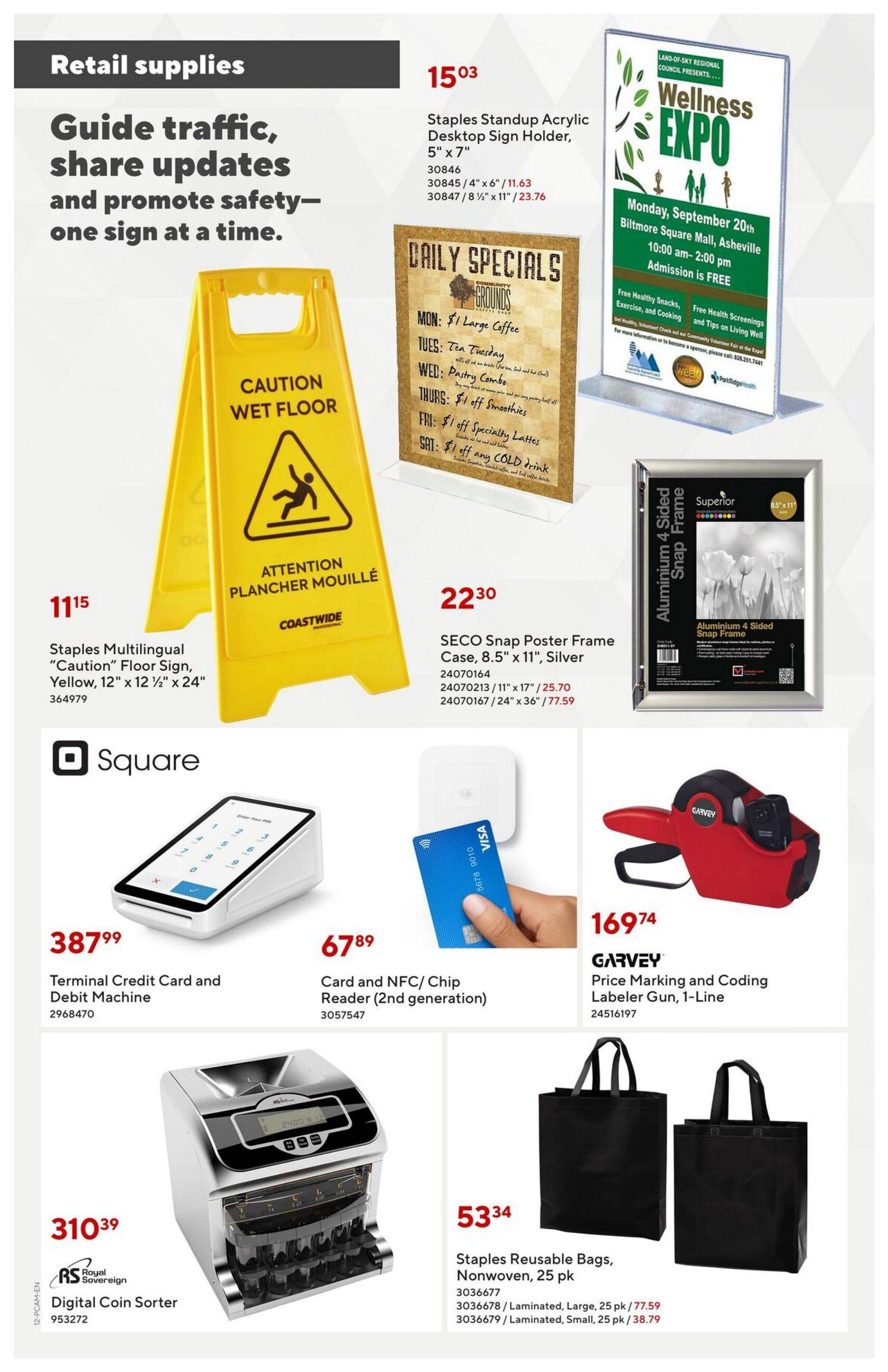 Staples flyer page 12 features retail supplies including a yellow 'Caution Wet Floor' sign for $11.15, a Staples Standup Acrylic Desktop Sign Holder for $15.03, and SECO Snap Poster Frame Cases starting at $22.30. Also available are a Square Terminal Credit Card and Debit Machine for $387.99, a Card and NFC/Chip Reader (2nd generation) for $67.89, a Royal Sovereign Digital Coin Sorter for $310.39, and Garvey Price Marking and Coding Labeler Gun for $169.74. The page also shows Staples Reusable Nonwoven Bags, 25 pk, for $53.34, with options for laminated large bags at $77.59 and laminated small bags at $38.79.