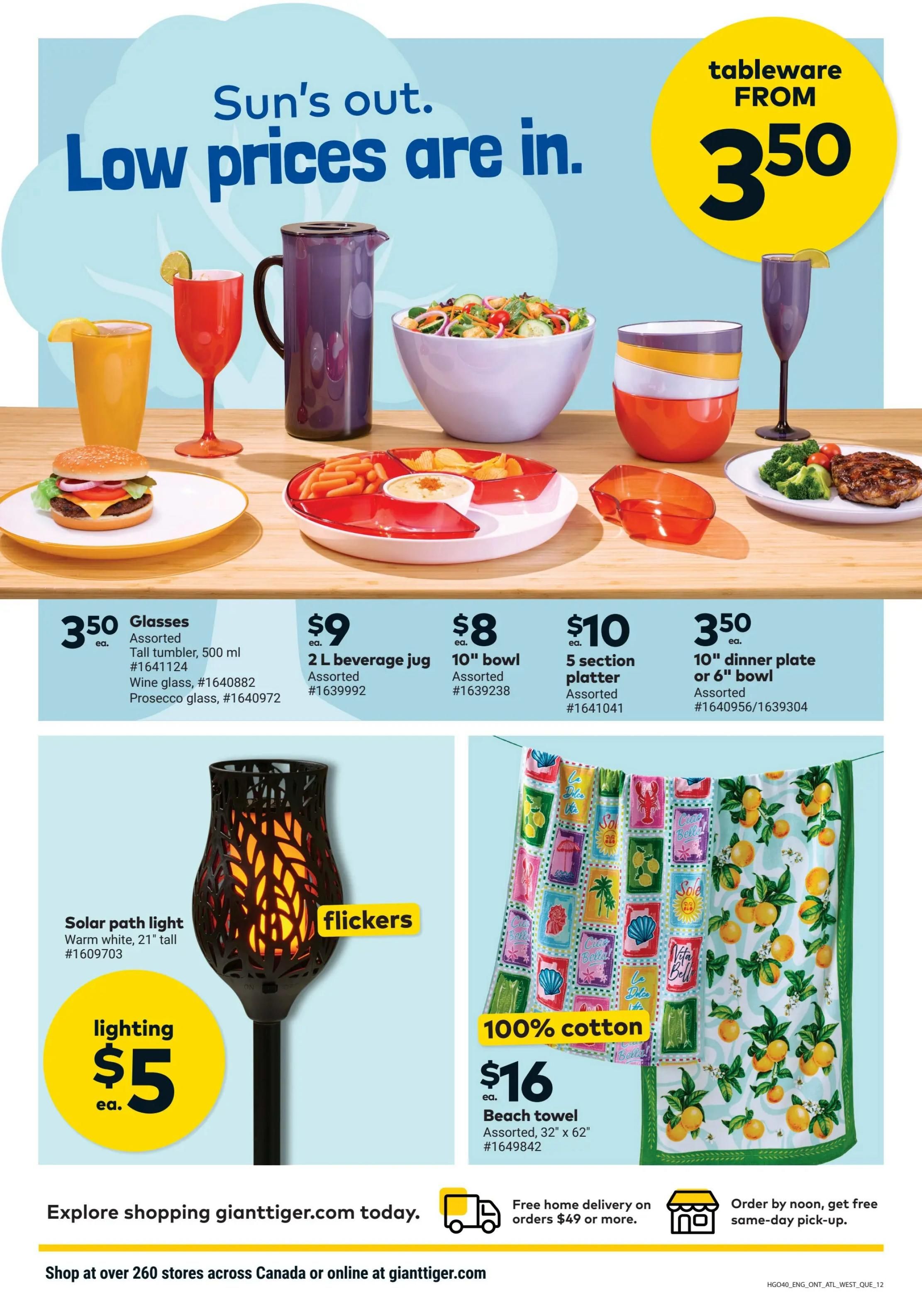 Giant Tiger flyer page featuring tableware and outdoor lighting. Tableware includes assorted glasses for $3.50 each, including tall tumblers (500 ml), wine glasses, and prosecco glasses. Also available are a 2 L beverage jug for $9, 10' bowls for $8, 5-section platters for $10, and 10' dinner plates or 6' bowls for $3.50 each. Outdoor lighting features a solar path light in warm white, 21' tall, for $5 each. A 100% cotton beach towel, assorted, measuring 32' x 62', is priced at $16 each. The page also highlights 'Sun's out. Low prices are in.' and 'tableware FROM $3.50'. Free home delivery is available on orders $49 or more, and same-day pick-up is offered by noon. Shop at over 260 stores across Canada or online at gianttiger.com.